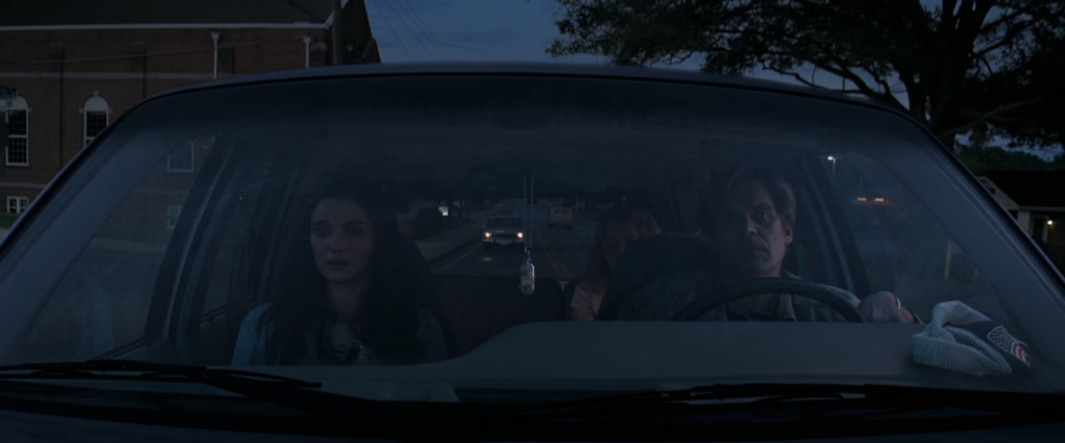 View of Alexei and Melina in car with brick building outside.
