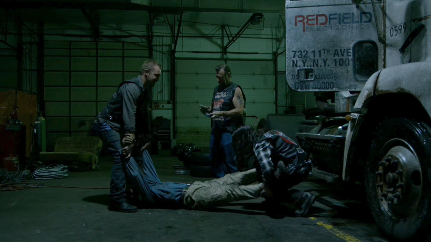 Men unload body from semi truck in Dogs of Hell warehouse.