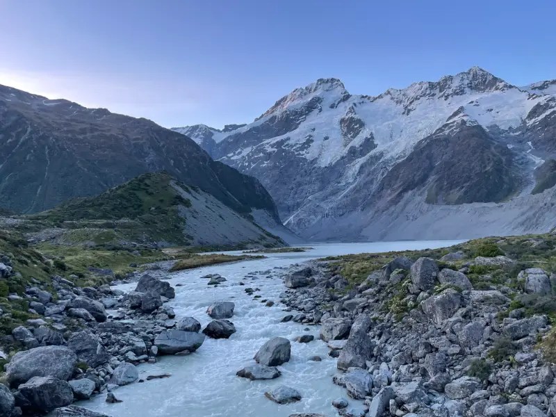 A rock filled river cuts through the center with snow capped mountains in the distance