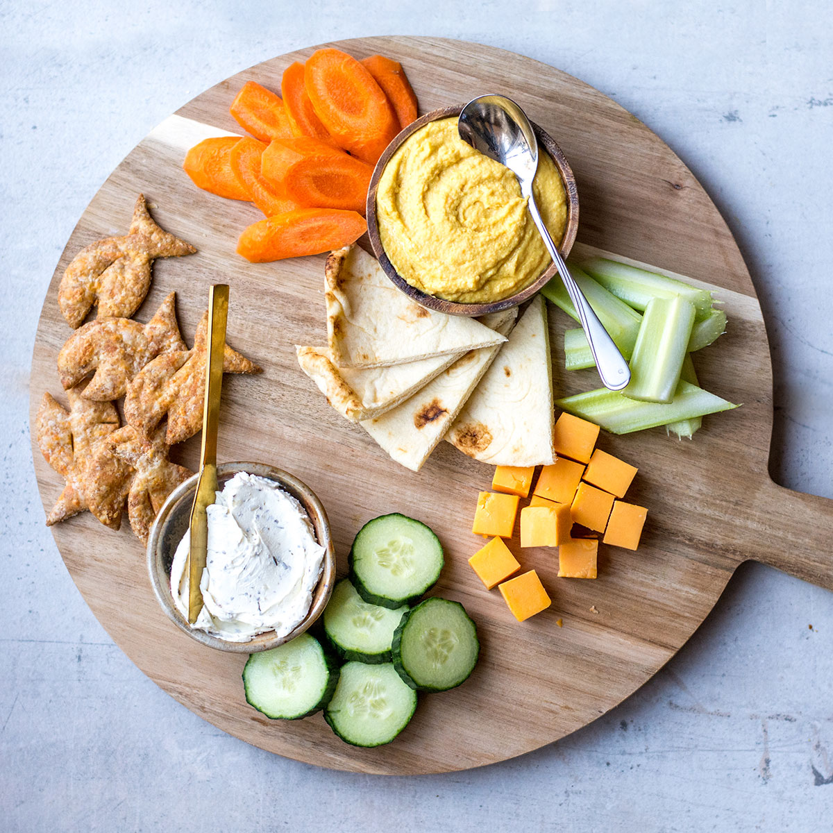 dips and cheese with pita on wooden platter with veggies