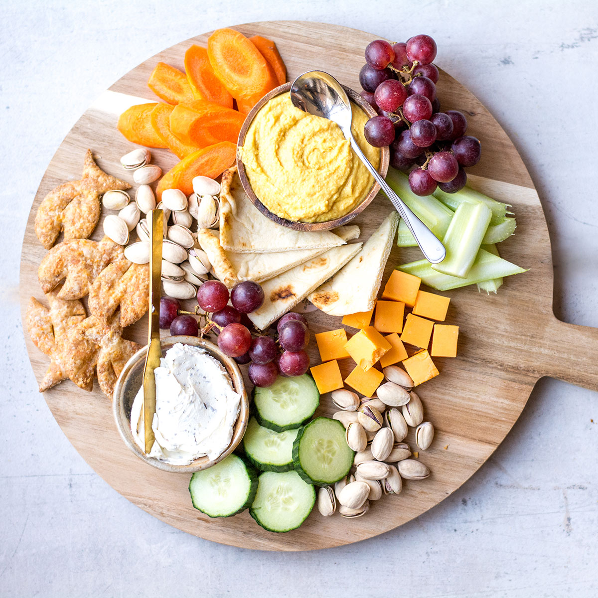 dips and cheese with pita on wooden platter with veggies and fruit