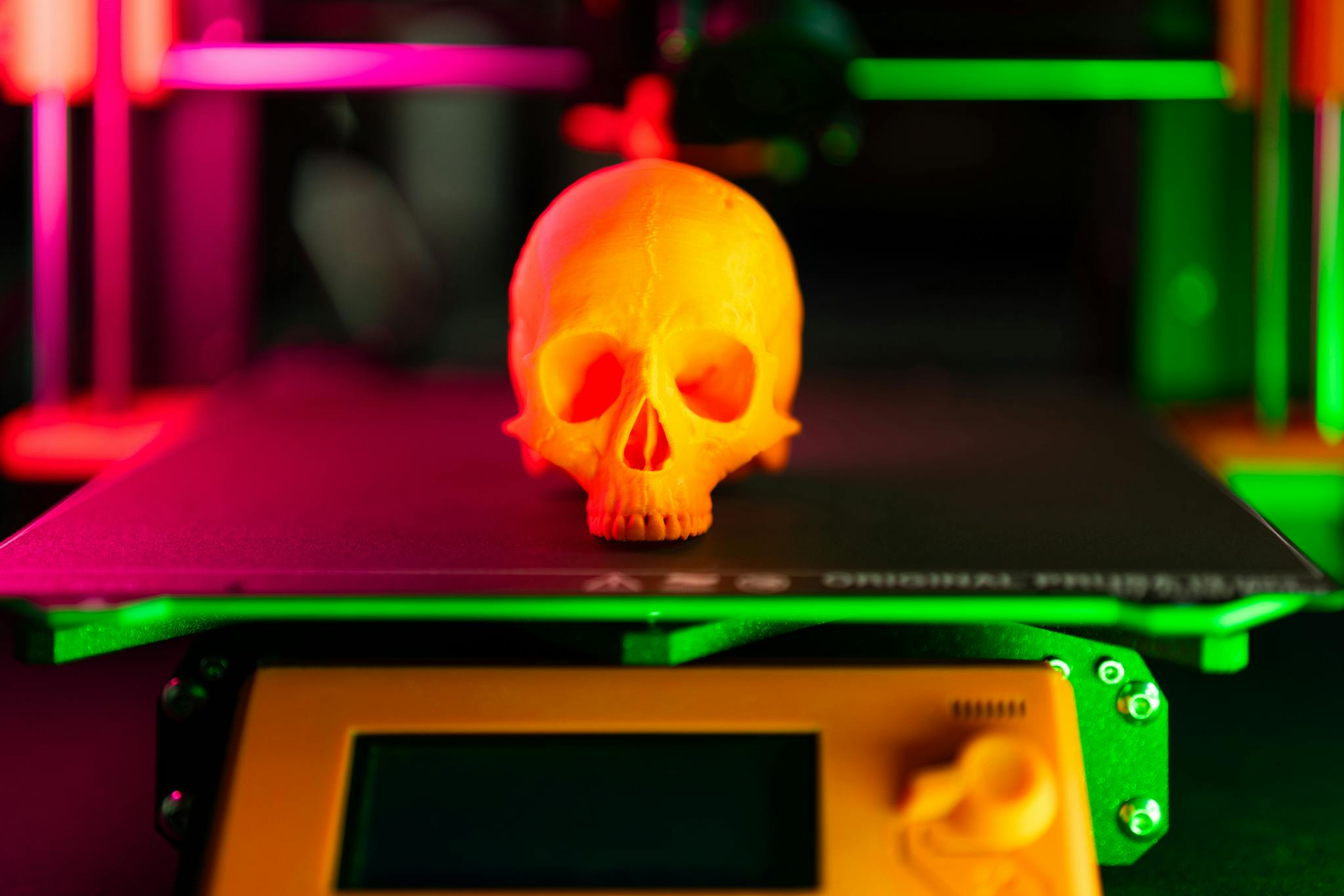 Close-up of an orange 3D-printed skull on a 3D printer with vibrant lighting.