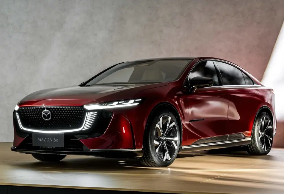 Un Mazda rojo visto desde la parte delantera izquierda en una sala de exposición, que destaca por su llamativa parrilla brillante, sus elegantes faros y sus modernas llantas de aleación.