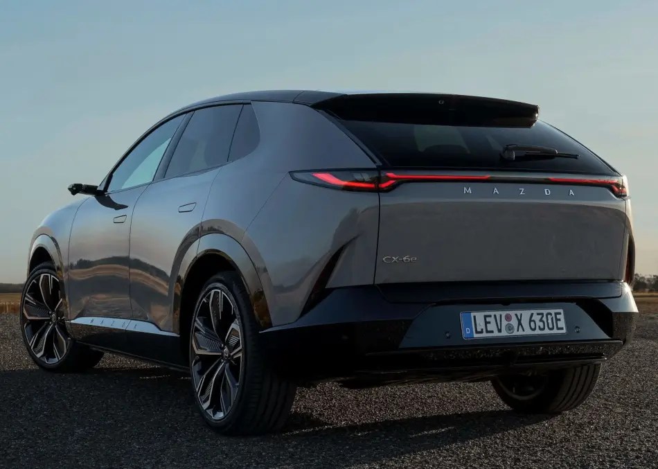Vista trasera de tres cuartos de un SUV Mazda CX-60e gris, aparcado en una carretera bajo un cielo despejado.