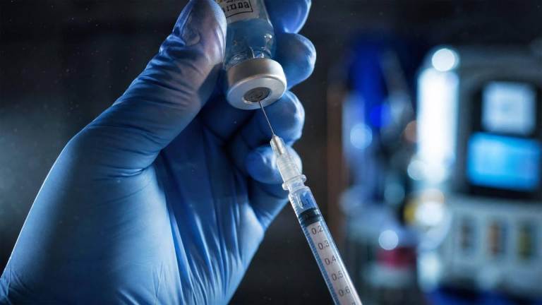 A gloved medical worker draws liquid from a small vial into a syringe in a clinical setting A gloved medical worker draws liquid from a small vial into a syringe in a clinical setting.