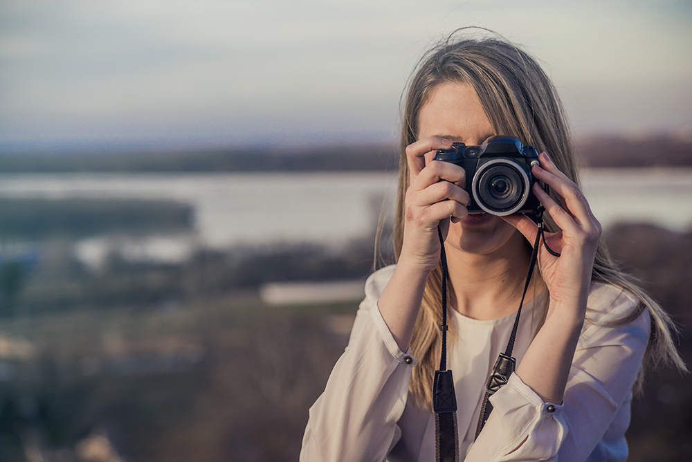 Photographer woman girl is holding dslr camera taking photographs. smiling young woman using a camera to take photo outdoors
