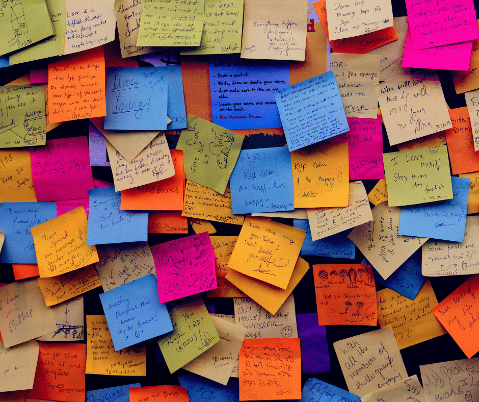 A wall covered in colourful handwritten sticky notes in pink, orange, blue, green and yellow, overlapping one another.