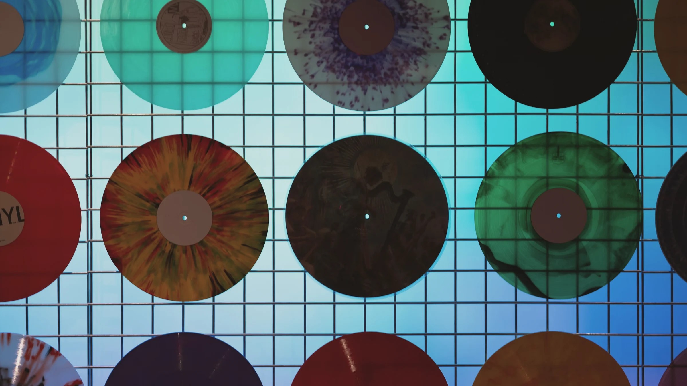 Colorful vinyl records displayed on a metal grid illuminated with blue light.
