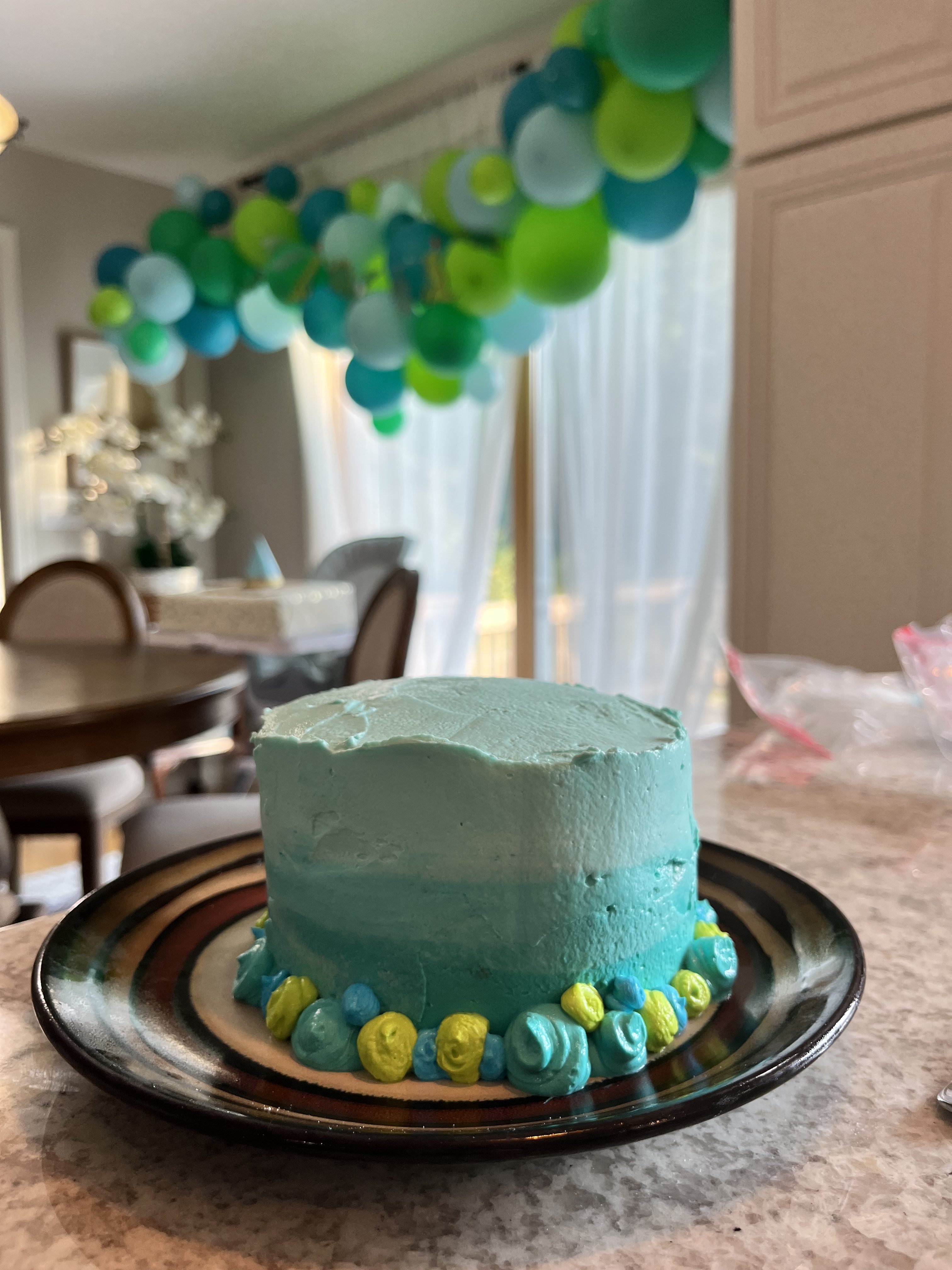 Blue smash cake on a plate with birthday balloons in the background