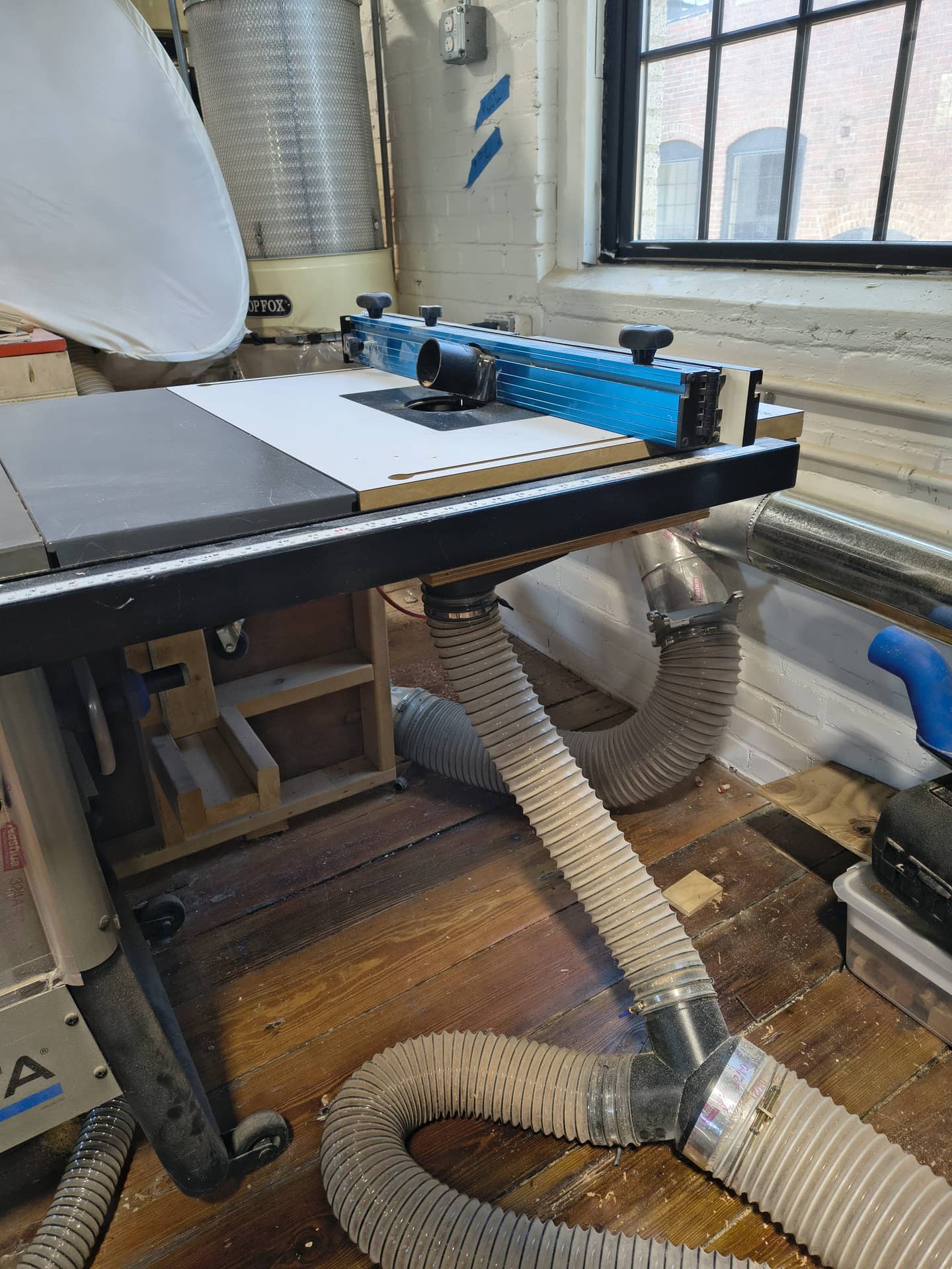 A bright blue beam on a white table attached to a metal shop saw bench with vacuum hoses attached underneath.
