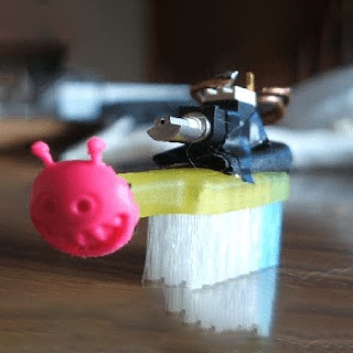 Tiny handmade bot from a toothbrush with pink creature head.