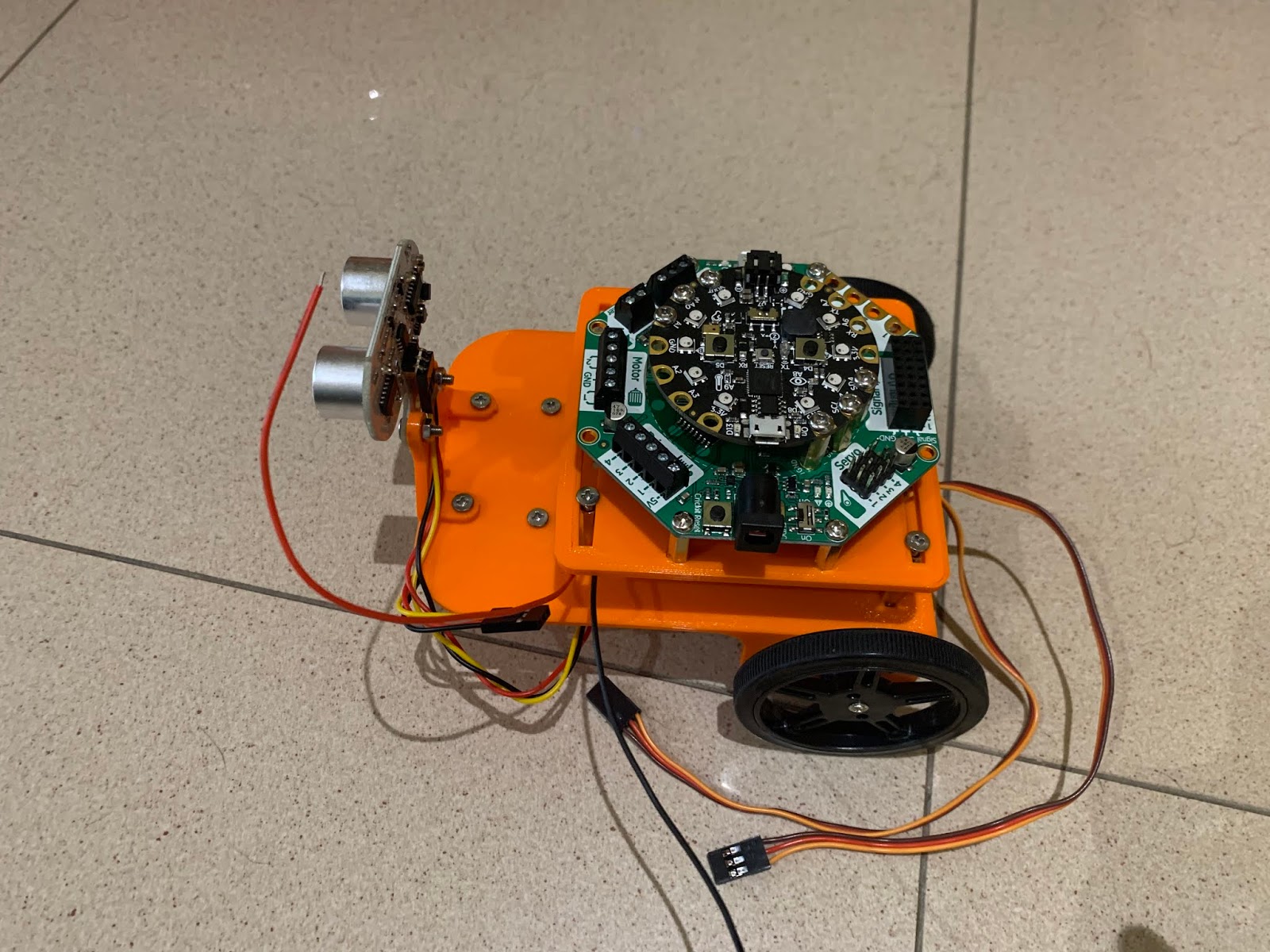 A small orange robot with eye-like silver sensors and a round circuit board on top.