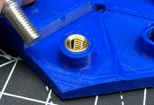 A bolt about to be installed into brass threaded insert set into a blue PLA hexagon.