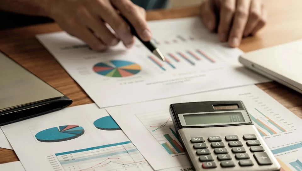 Professional reviewing financial reports with charts and calculator on desk.