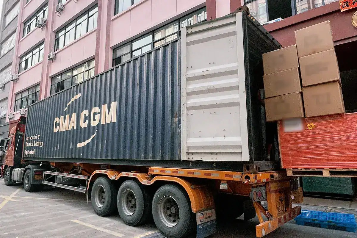 Cartons and a wrapped pallet being loaded into a shipping container outside a Minden Intl warehouse