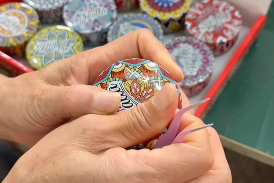Close check of a printed tin lid with tweezers, taken from a tray of finished decorative tins