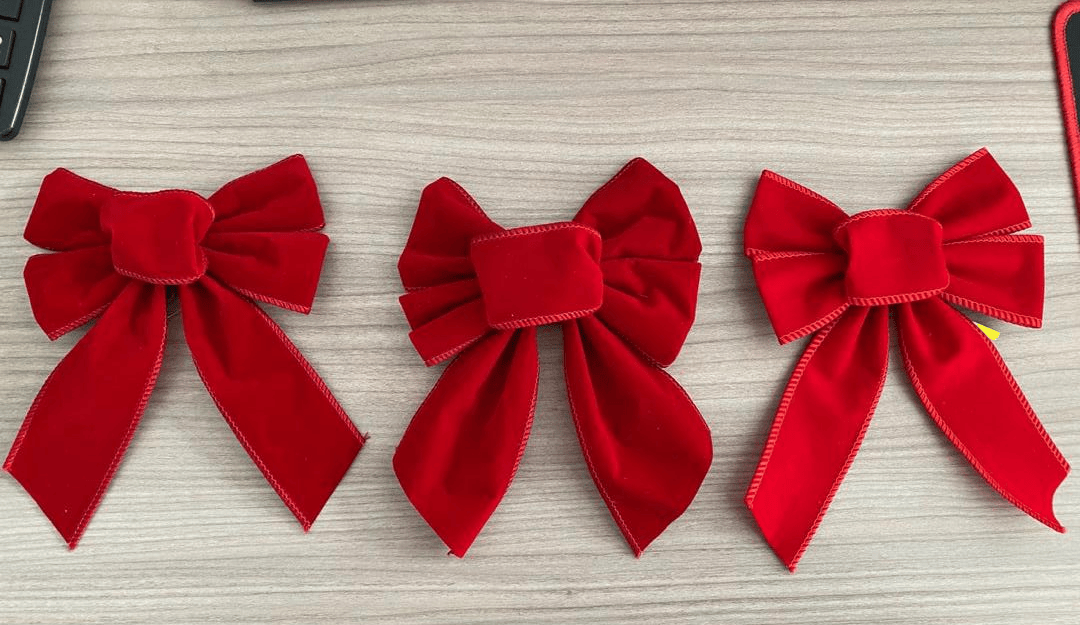 Three red velvet Christmas bow samples of different sizes compared side by side on a desk