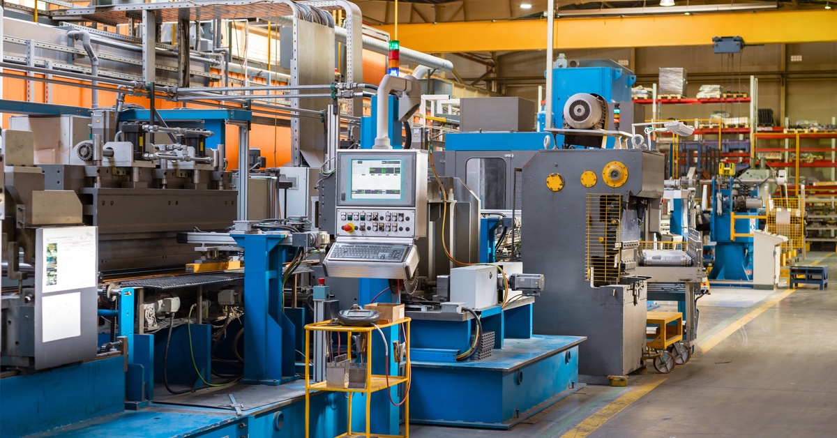 A complex metal-working machine with a screen and control panel takes up a large amount of space in a manufacturing facility.
