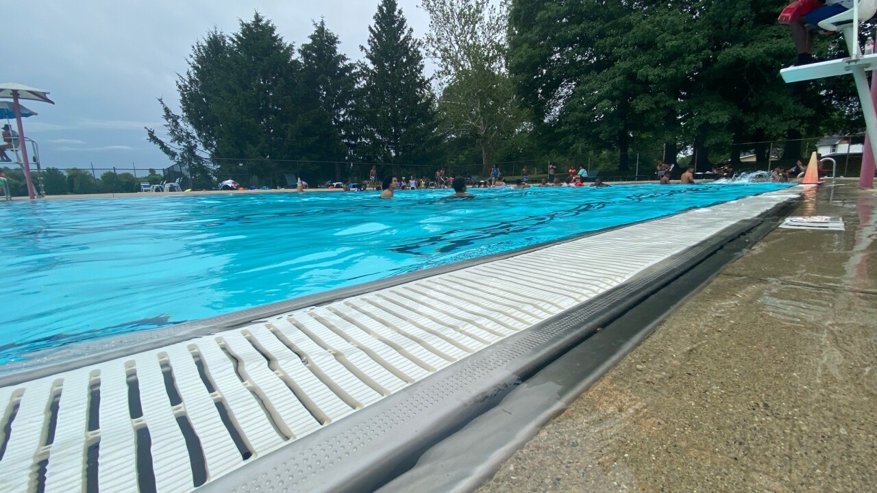 An outdoor pool on a sunny day, with people playing in it.