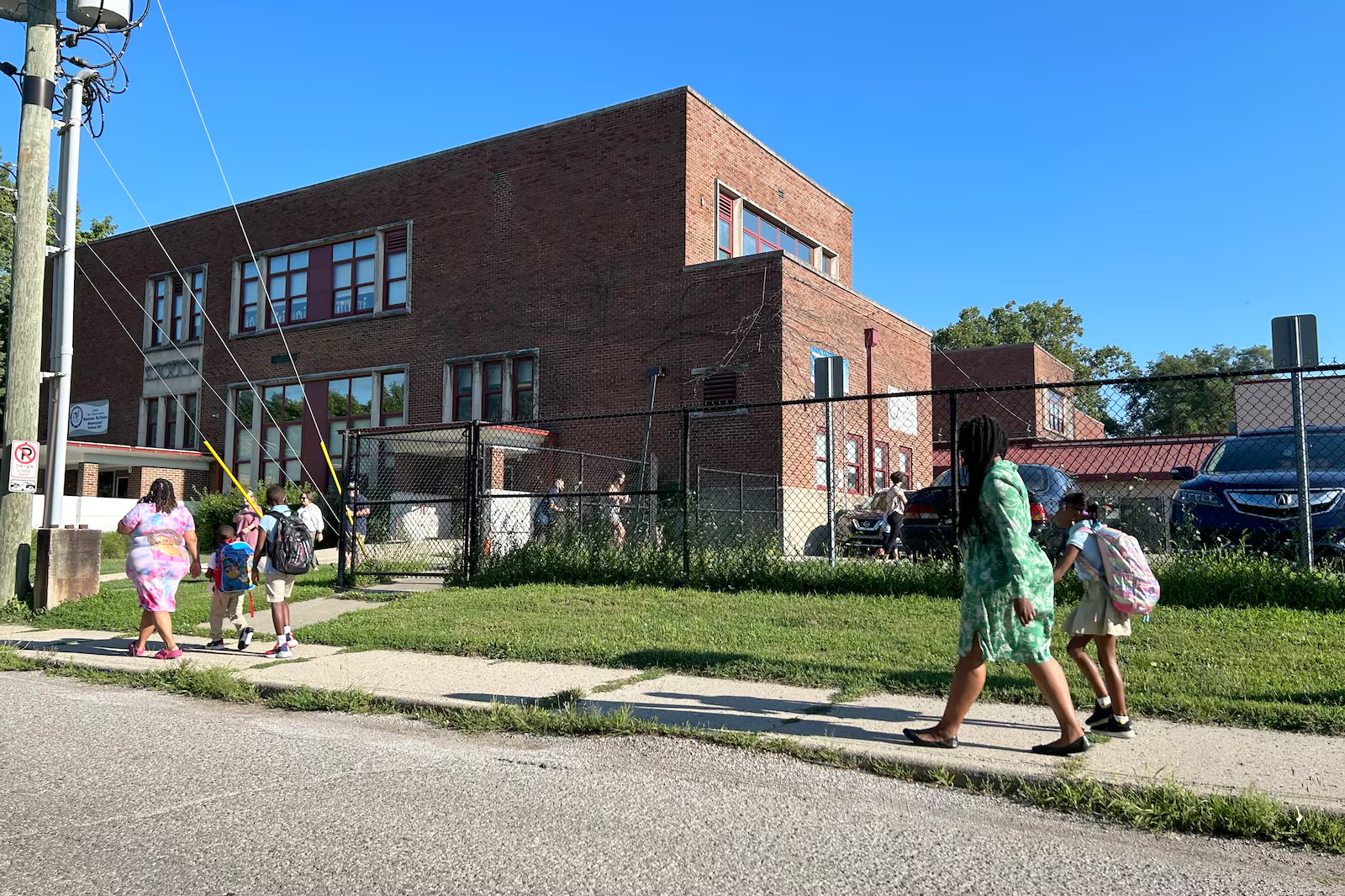 Parents and children hold hands while walking into a brick school building.