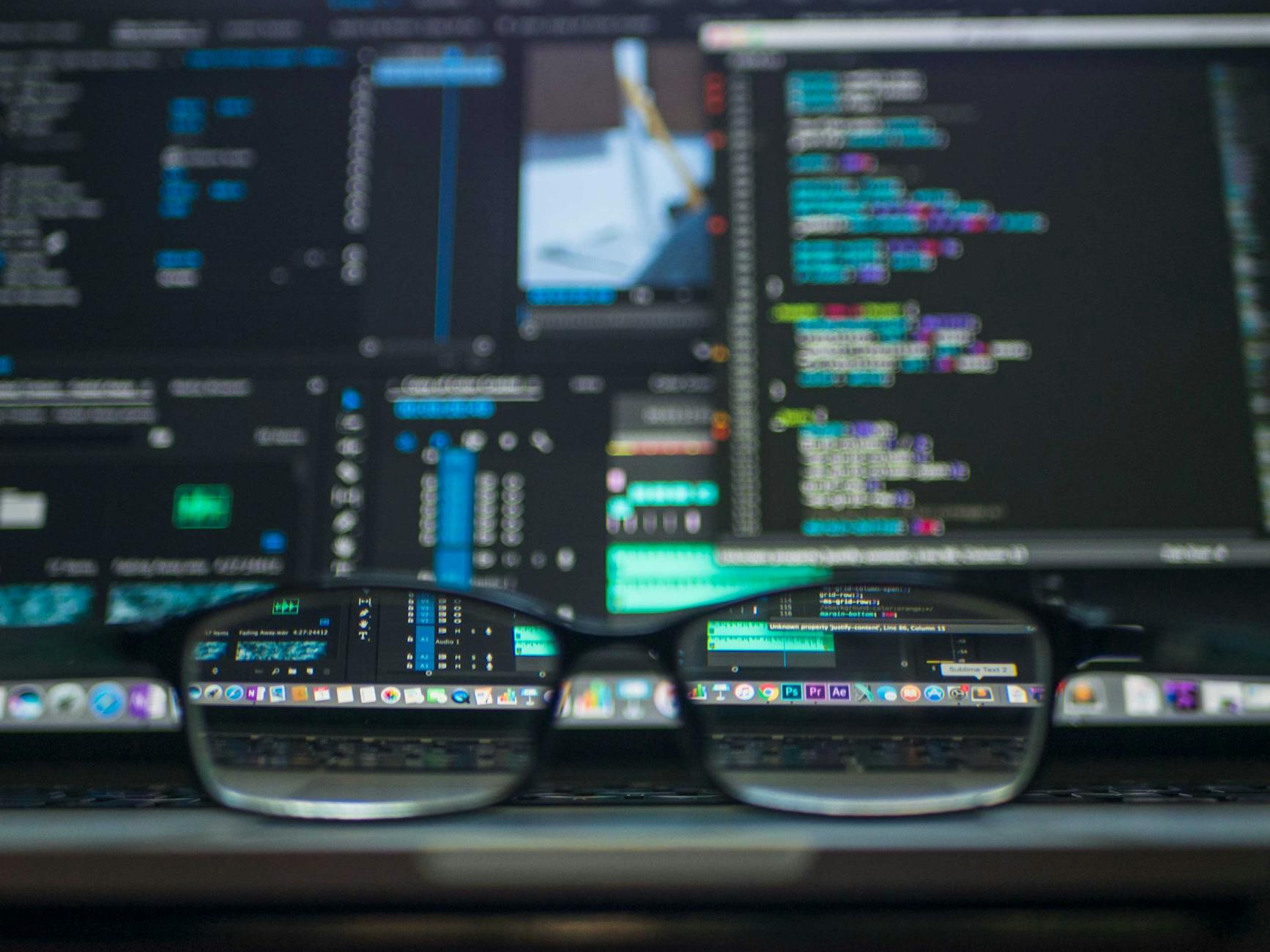 A person working on a laptop with code on multiple screens in a home office setting.