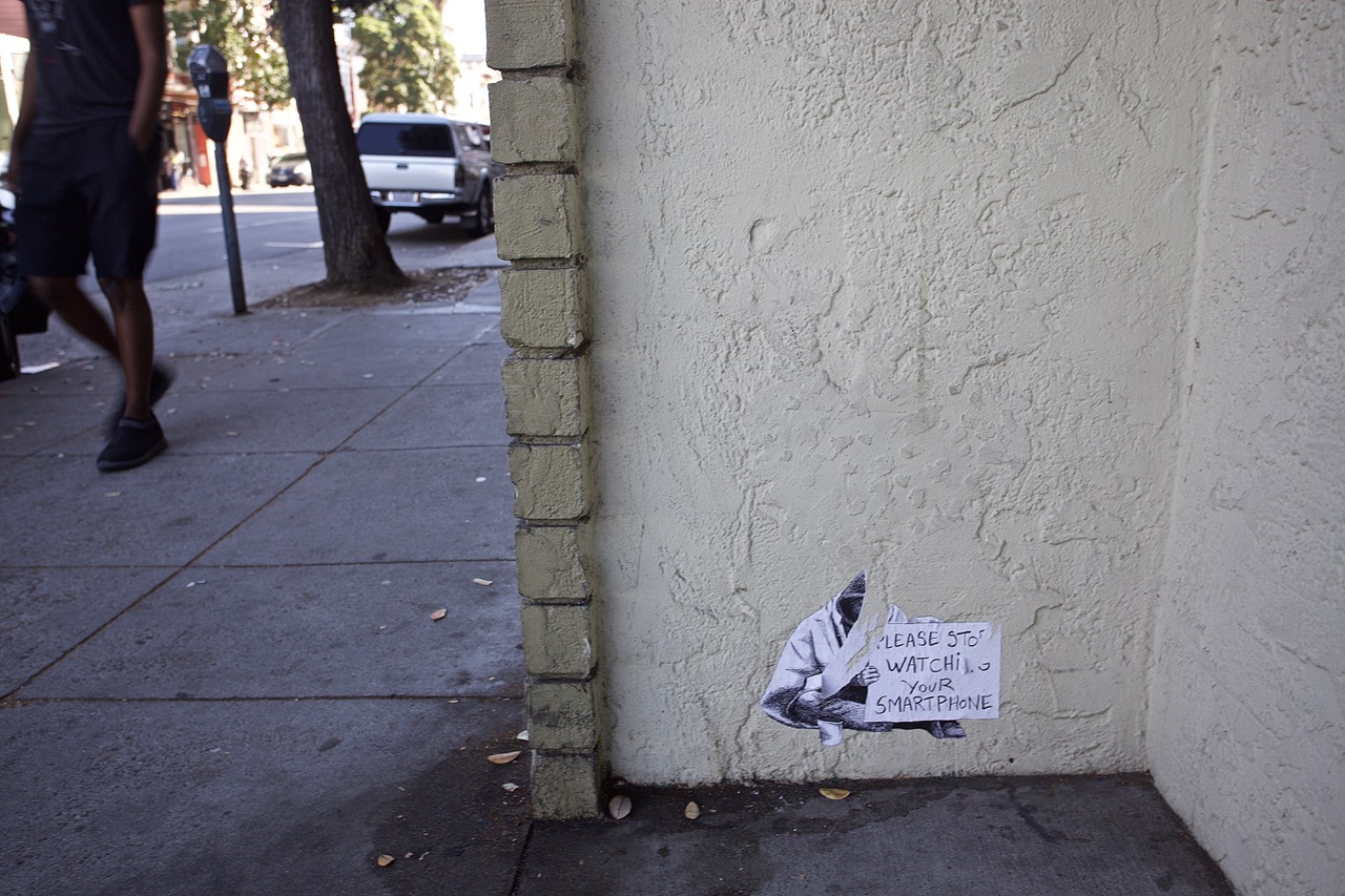 Small stencil on a corner wall telling people to get off their cell phones.