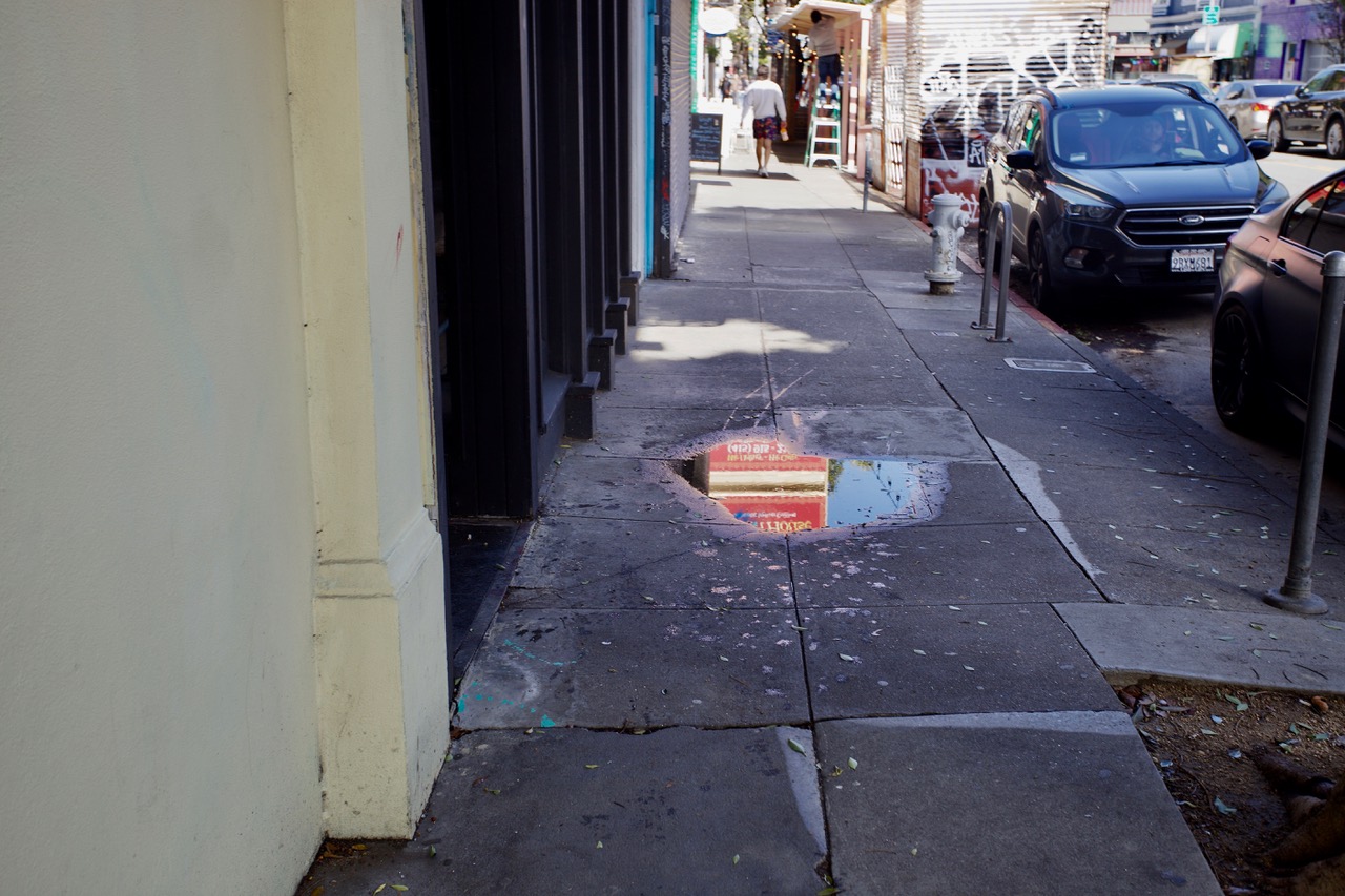 A puddle of water in the middle of an urban sidewalk.