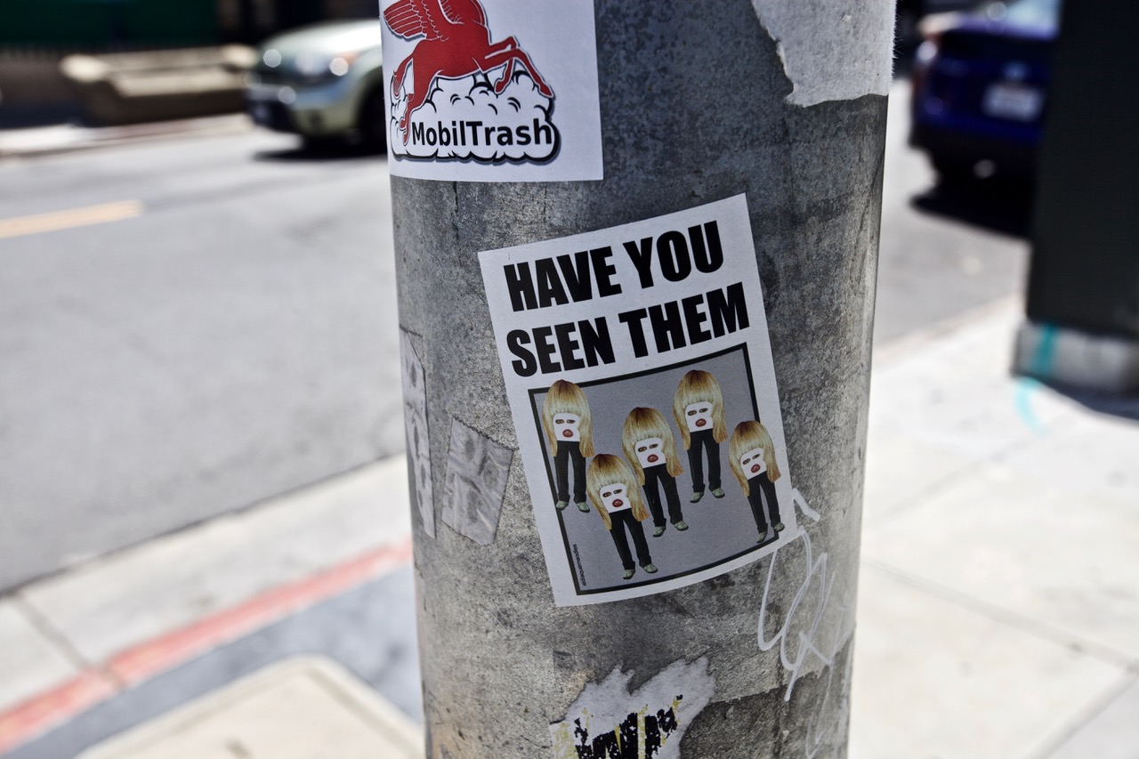A flyer taped to a service poll with writing and five figures with their faces scratiched out.