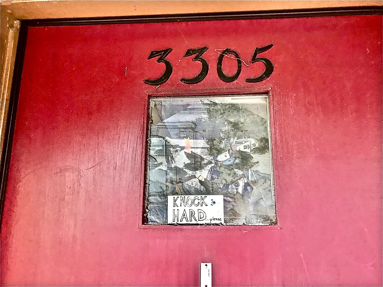 A red door with the numbers 3305, the window is covered with newspaper.