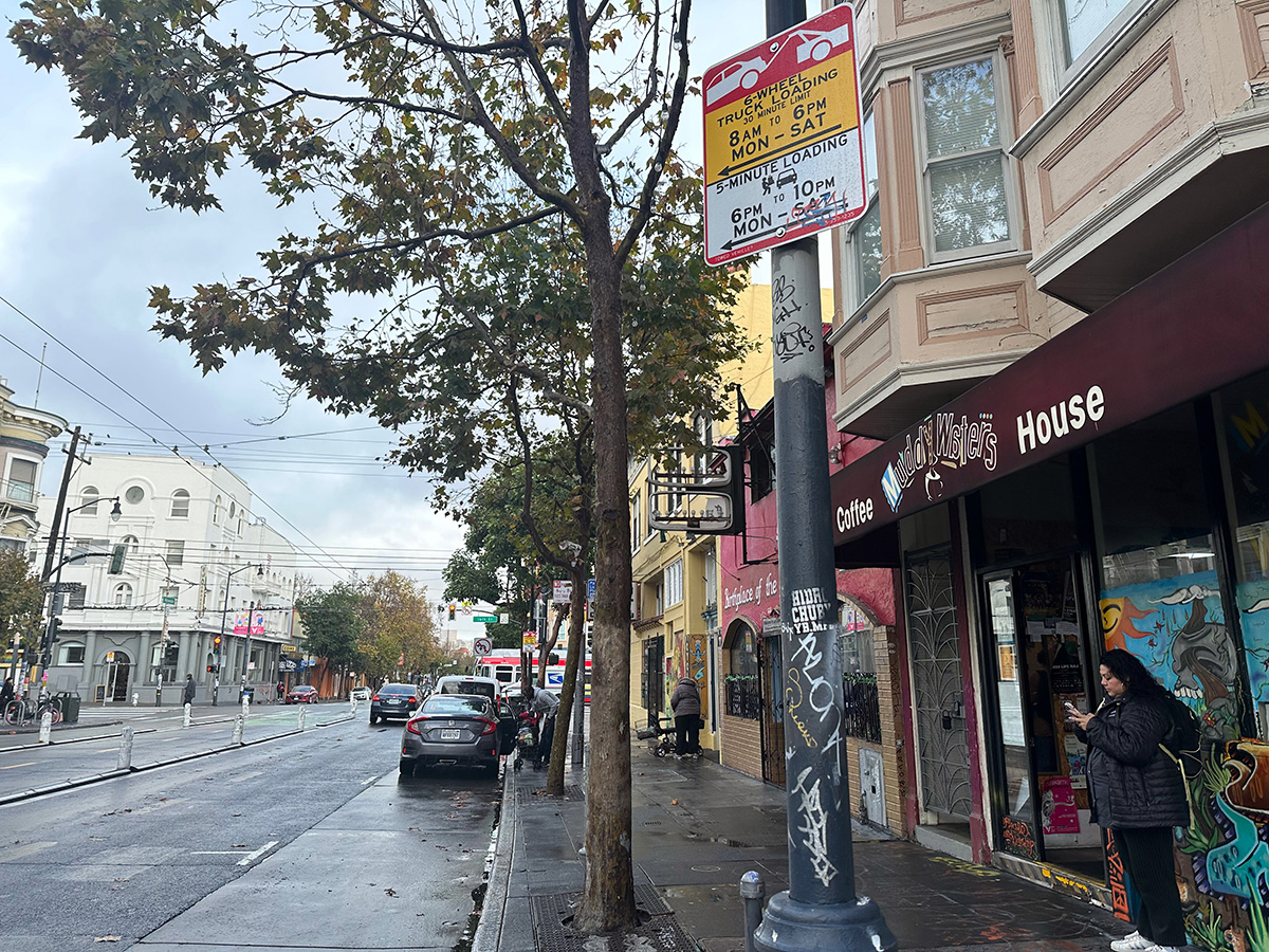 A woman is standing on a sidewalk next to a store.