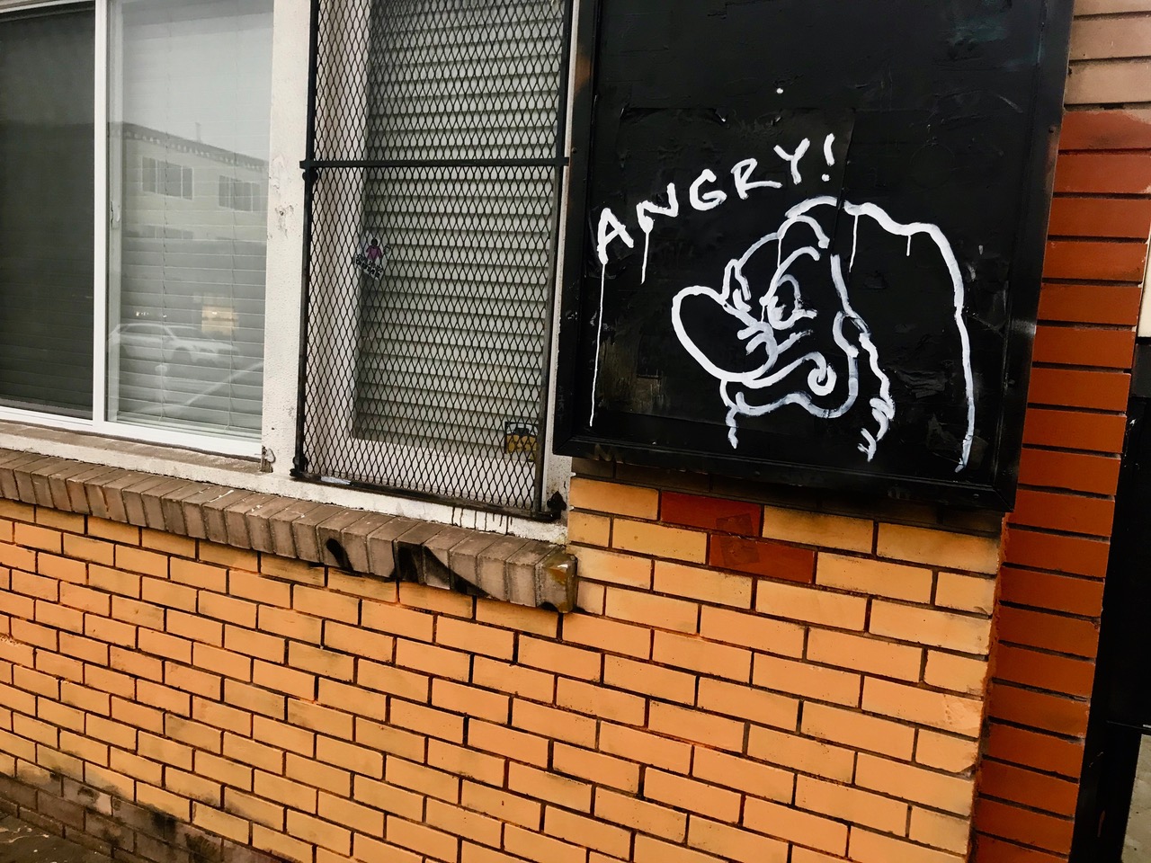 A building with a spray-painted sketch of a dwarf on the side of it with the word ANGRY!