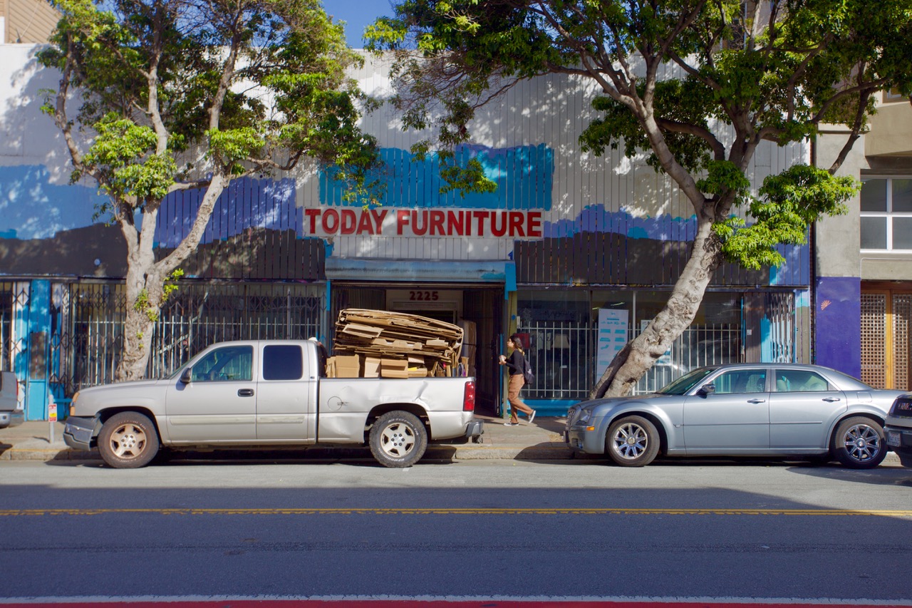 Pickup truck loaded with wooden planks parked in front of a store called Today Furniture.