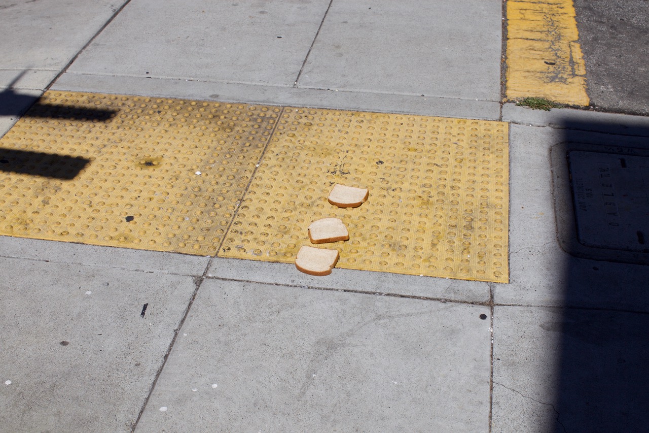 Three slices of white bread are lying on a yellow textured sidewalk curb ramp near a street corner.