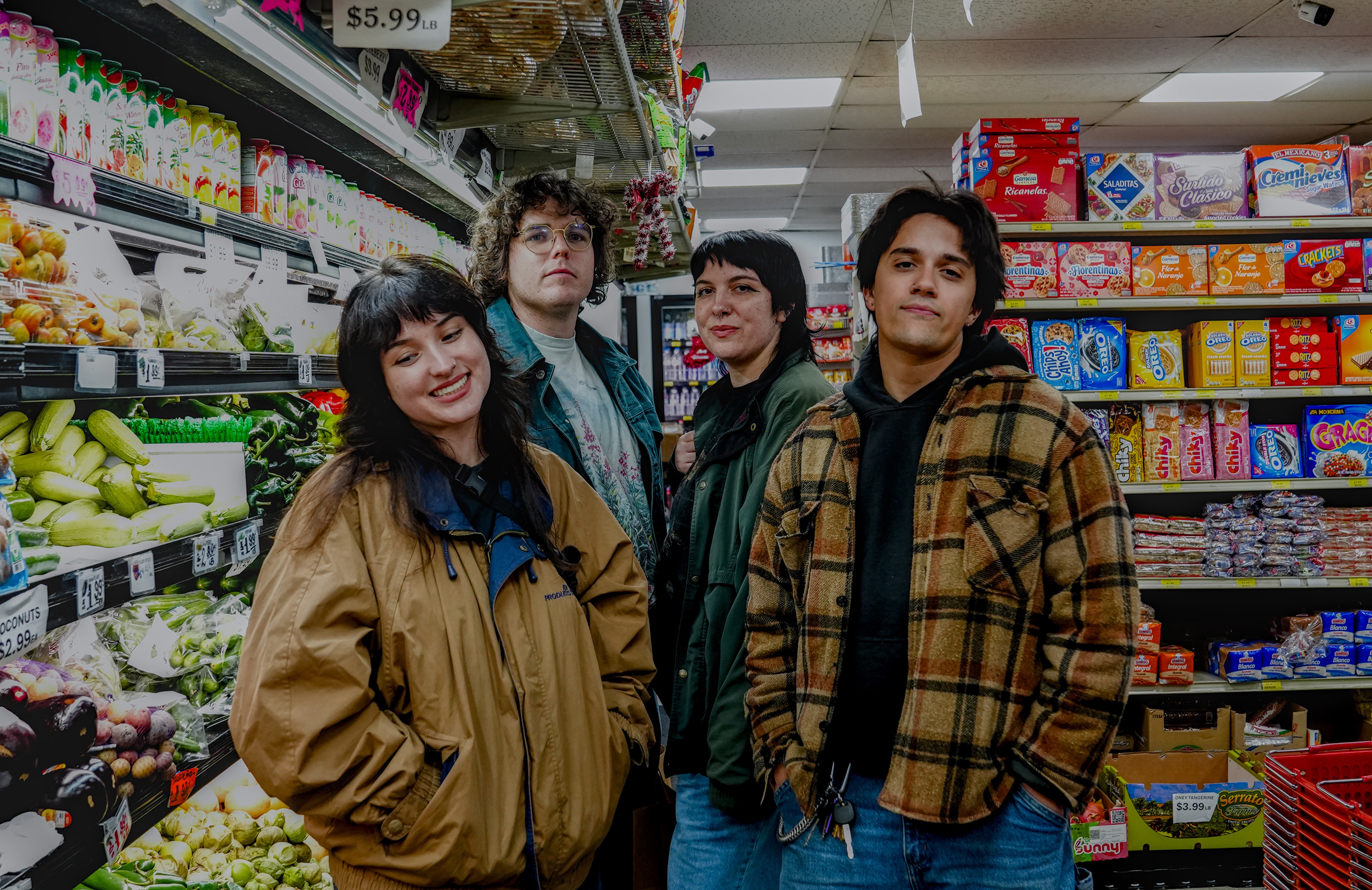 Four people stand together in a grocery store aisle near produce and packaged goods, looking at the camera.