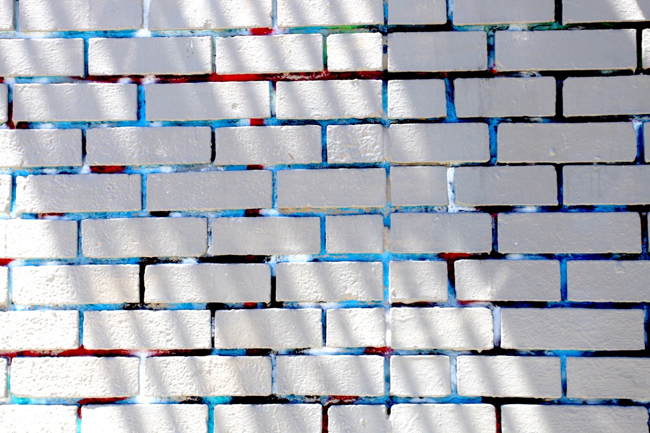White brick wall with blue and red mortar lines, showing diagonal shadows cast across the surface.