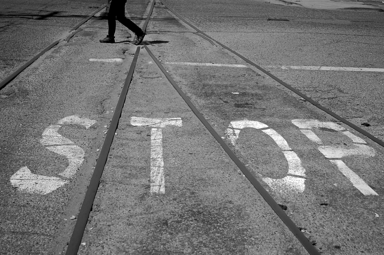 A person walks across train tracks where the word “STOP” is painted in large white letters on the pavement.