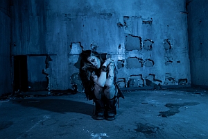 A person crouching in a dimly lit, weathered room.