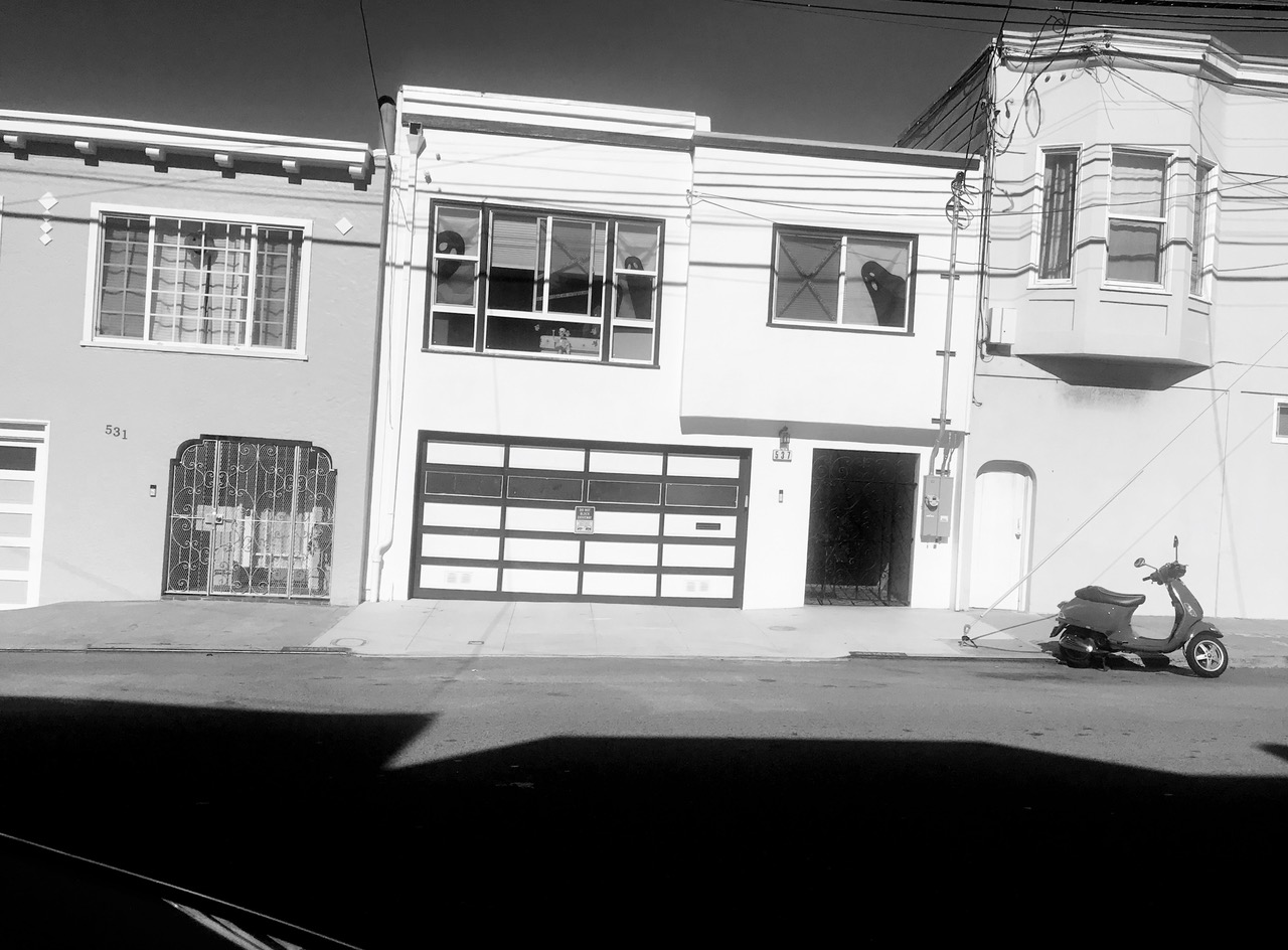 A row of townhouses in black and white, featuring a parked scooter and two ghost decorations in an upper-story window.