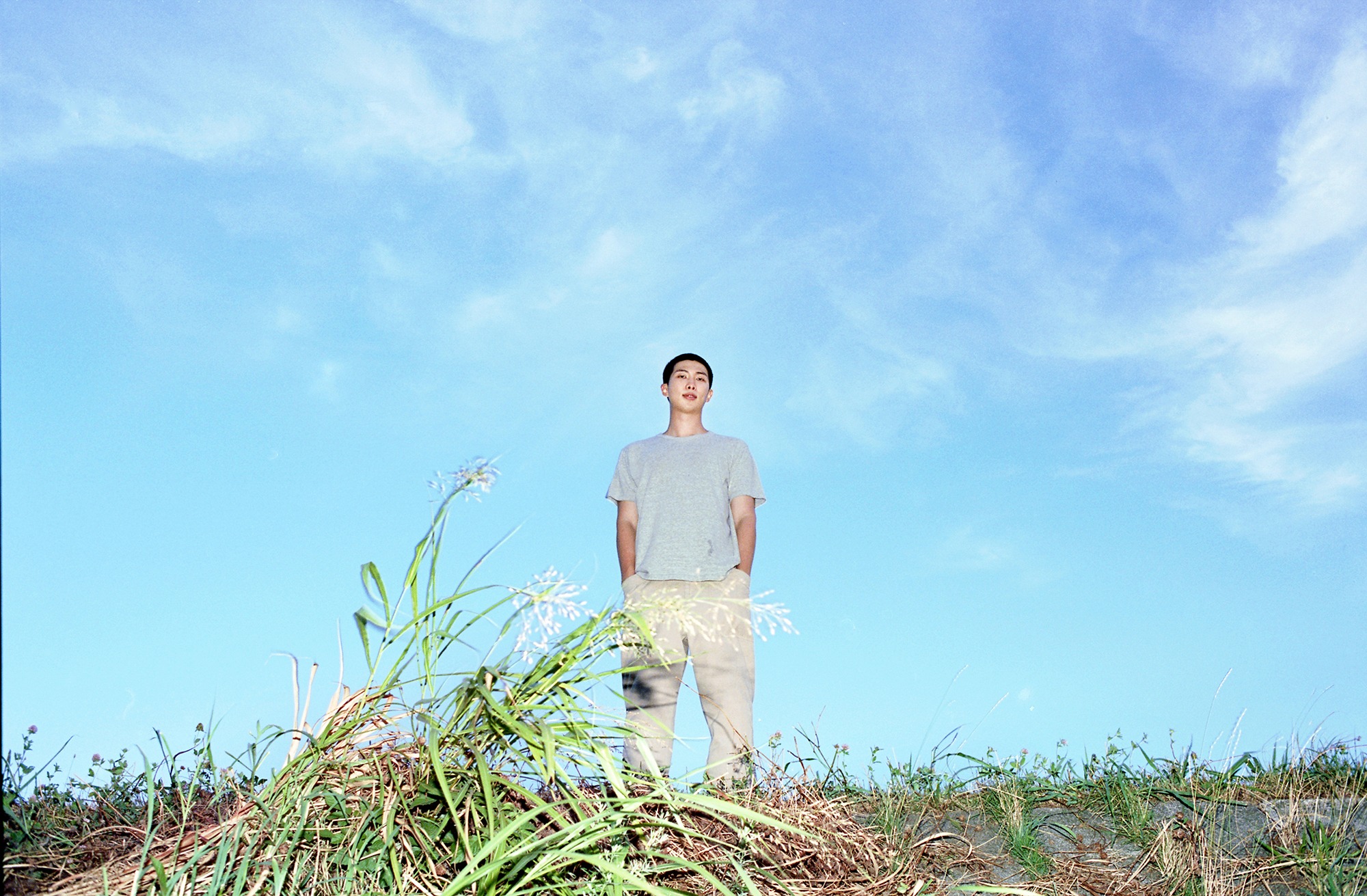 A person stands on grassy ground under a clear blue sky, wearing a grey t-shirt and light-colored pants.