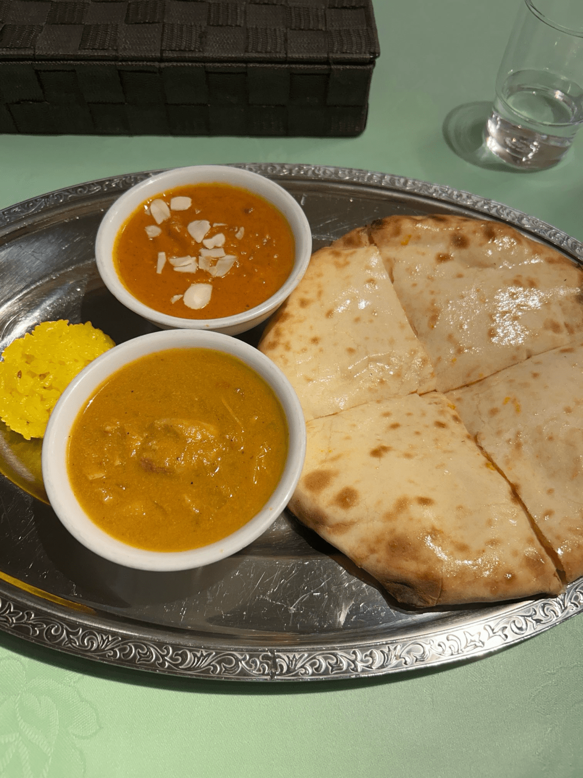 Indo-Nepal curry set in Japan with butter chicken curry, dal curry topped with sliced almonds, saffron rice, and freshly baked naan on a silver platter.