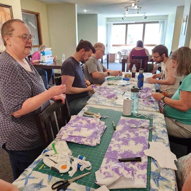 Volunteers work with fabric, scissors, and other tools around two tables.