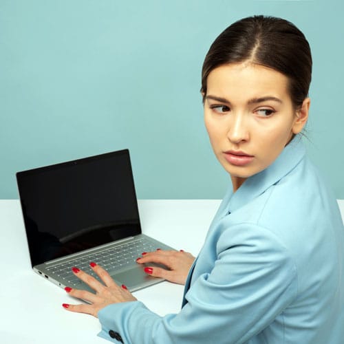 A pretty girl types on her laptop in front of her but looks over her shoulder for anyone watching. MNK