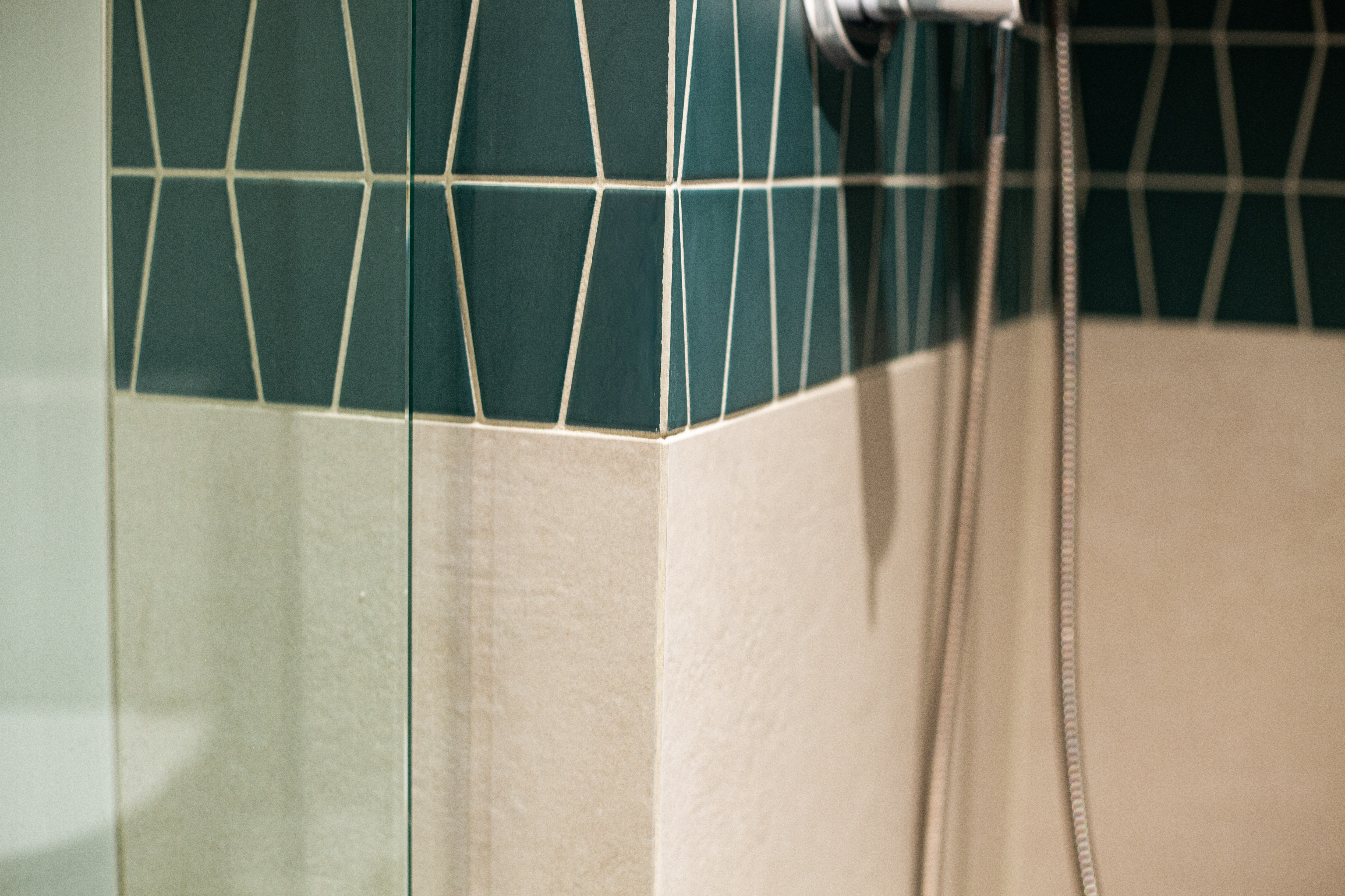 Detail of geometric teal shower tile meeting pale large-format wall tile