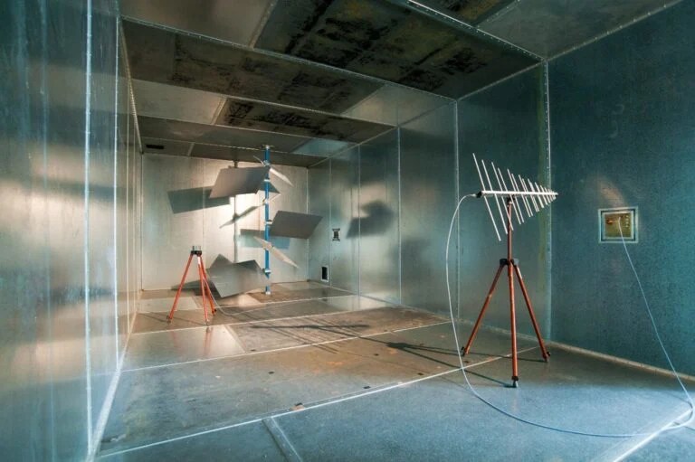 RF EMC testing in a reverberation chamber with metallic stirrers and directional antenna, used for simulating multipath propagation in shielded environments.