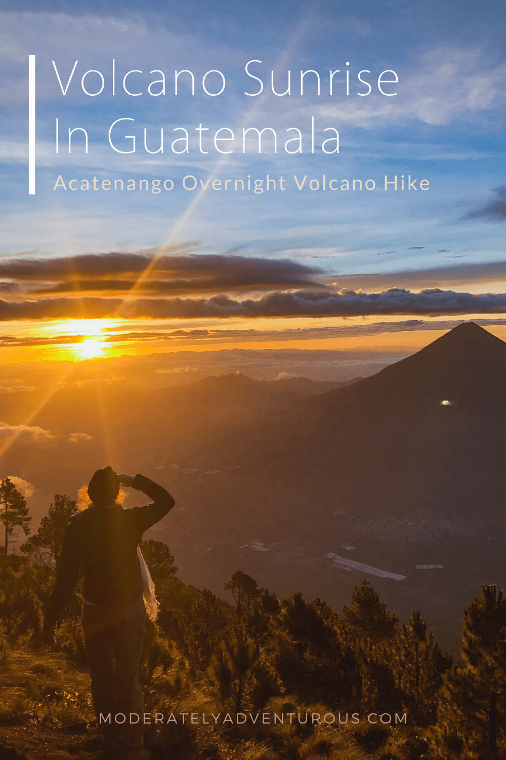 The sun rises behind holds her hand over her eyes to see out over the Augas Volcano while her scarf catches the wind and she stands on the Acatenango Volcano. Text on the image reads, "Volcano Sunrise in Guatemala, Acatenango Overnight Volcano Hike." Moderately Adventurous Travel.