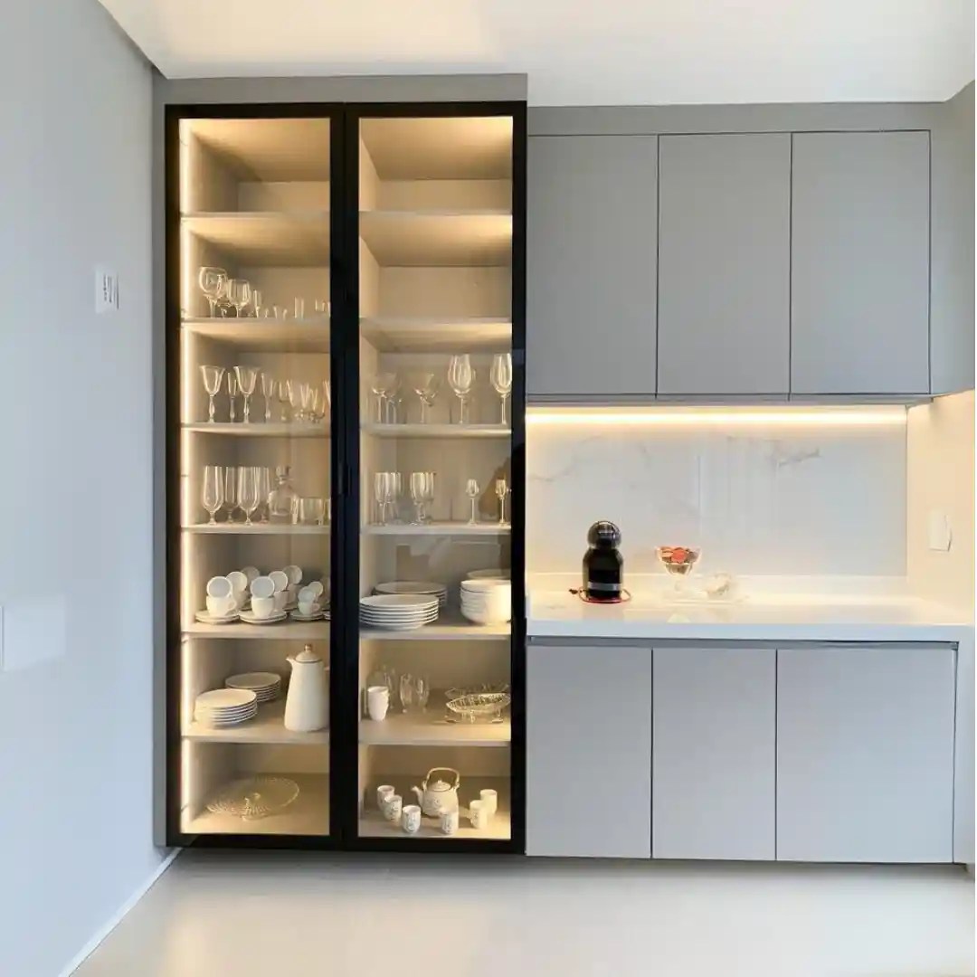 Modern kitchen with illuminated glass cabinet displaying dishes and glasses.