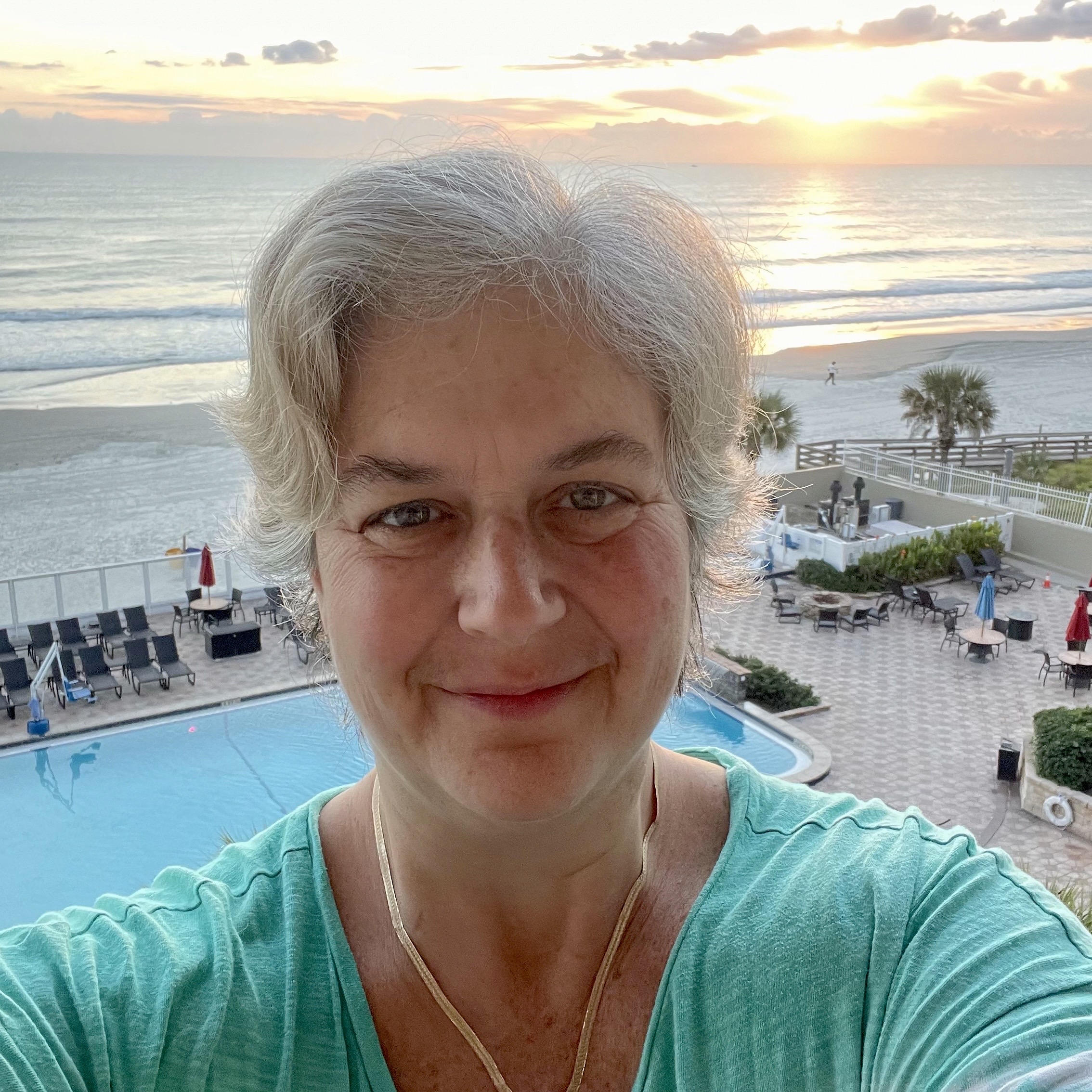 Lyssa on a balcony with sunrise over a beach behind her.