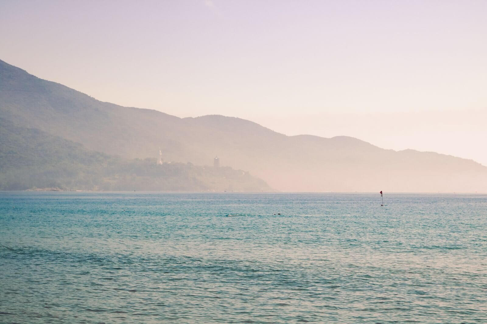 Peaceful scene of Vietnam's coastline with mountains in the background, captured at sunrise.