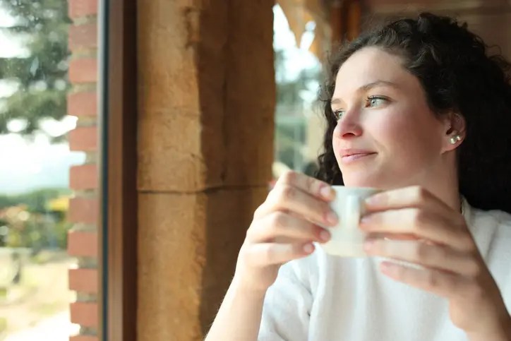 Woman calmly reflecting while holding a cup of coffee, illustrating how to practice mindful spending to save money.