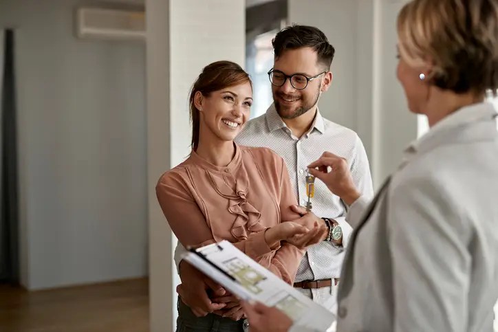 A smiling couple receiving house keys from a real estate agent, symbolizing how to navigate rising housing costs when buying a home.